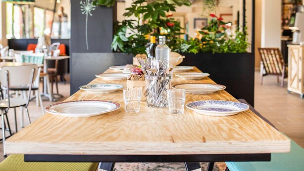 Een restaurant met een lange houten tafel, gedekt voor een maaltijd, omringd door stoelen.