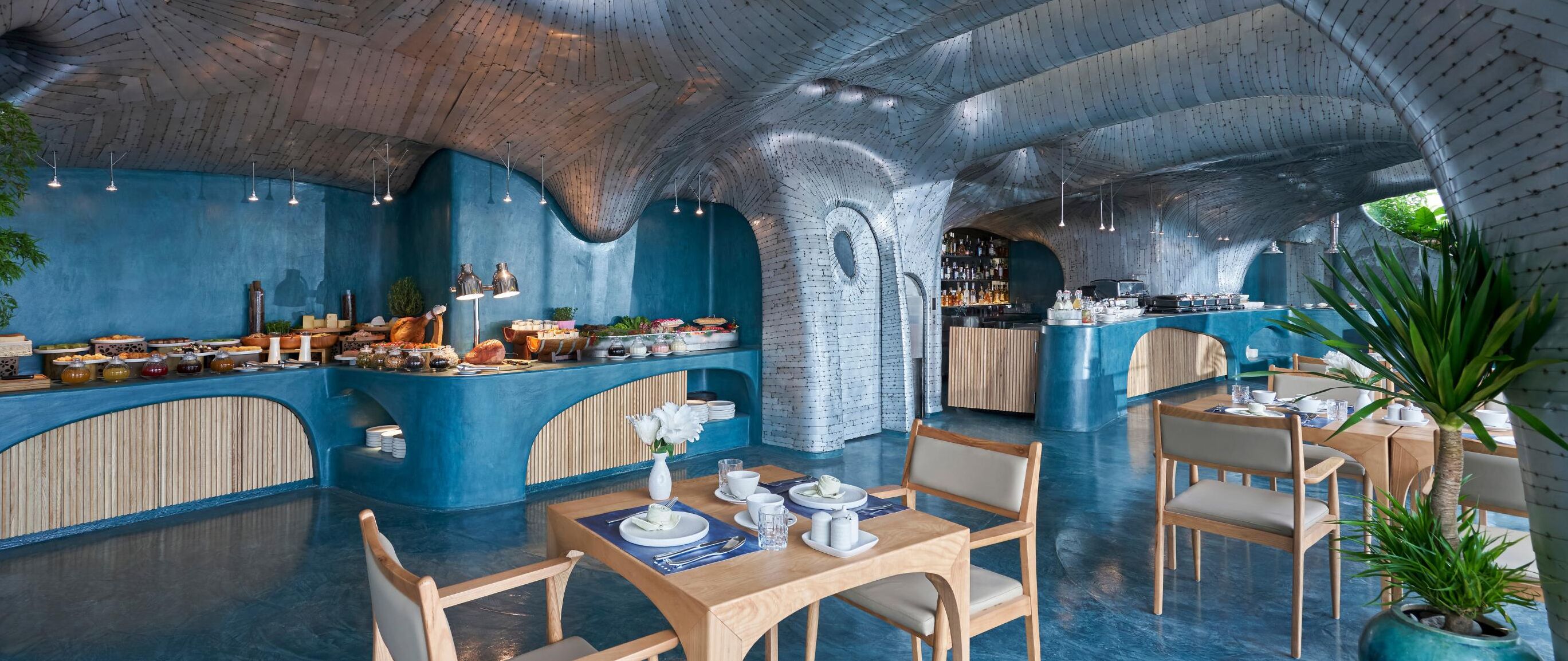A restaurant with a unique arched ceiling and blue walls, featuring a buffet area with various dishes and a seating area with tables and chairs.