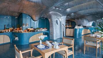 A restaurant with a unique arched ceiling and blue walls, featuring a buffet area with various dishes and a seating area with tables and chairs.