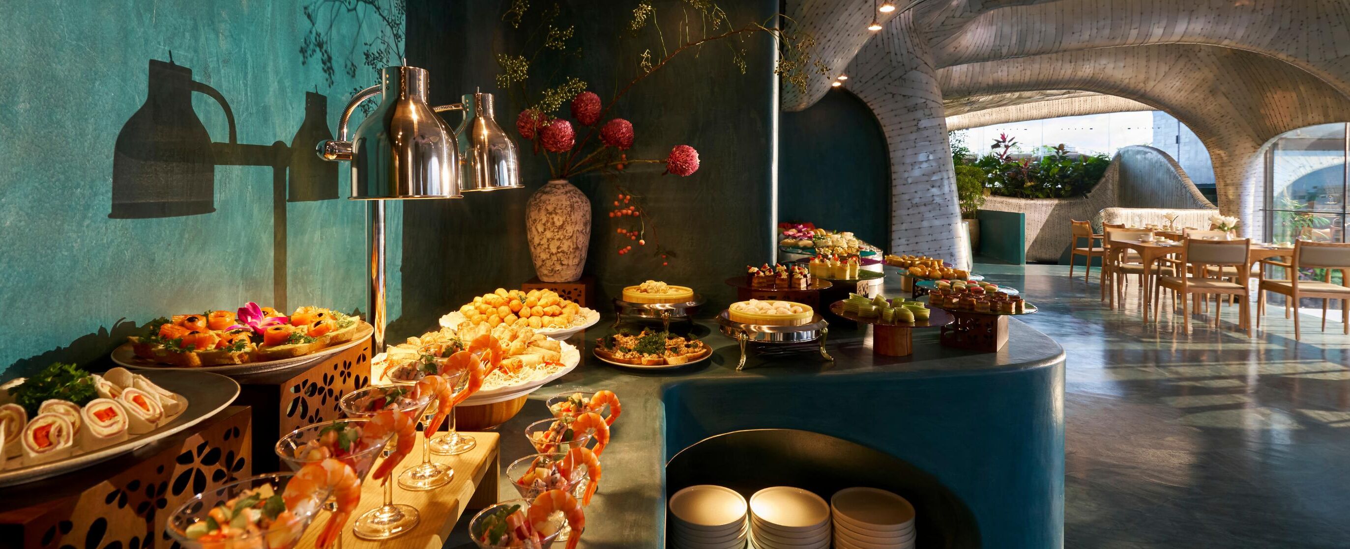 A buffet with various dishes and drinks, a decorative vase with flowers, and a seating area with tables and chairs.