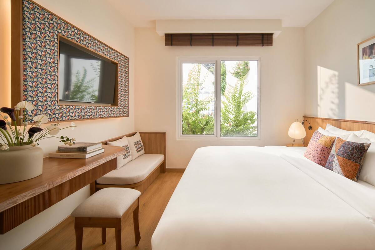 Habitación de hotel con una cama grande, un escritorio con un florero, un televisor y una ventana con vista a follaje.