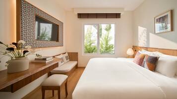 Habitación de hotel con una cama grande, un escritorio con un florero, un televisor y una ventana con vista a follaje.