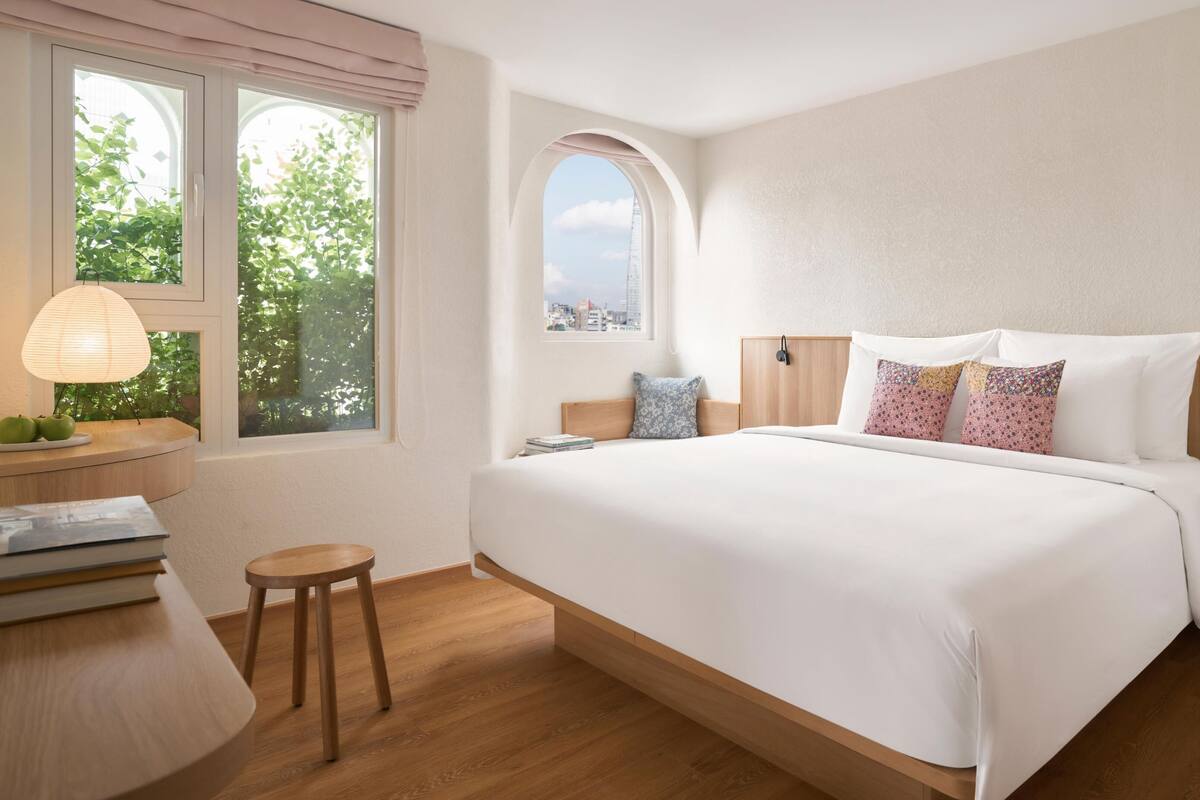 Un dormitorio moderno con una cama grande, una mesita de noche con lámpara y vistas a zonas verdes a través de la ventana.