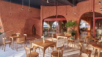 An indoor dining area with brick walls, wooden tables and chairs, and potted plants.