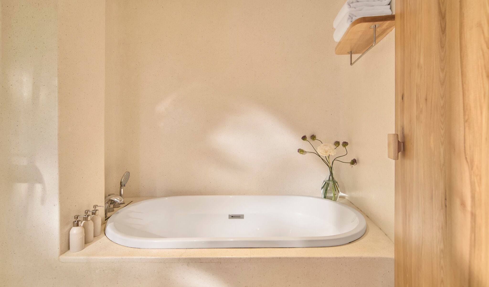 A bathroom with a freestanding bathtub, a small sink, and a wooden shelf with a towel.
