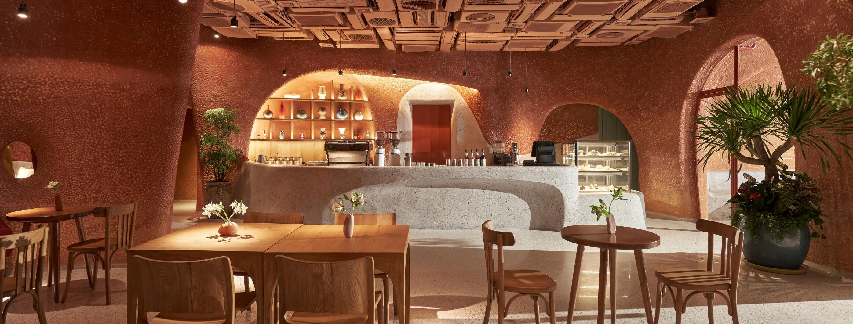 A cozy restaurant with a rustic brick wall, wooden tables and chairs, and a central counter with a coffee machine.