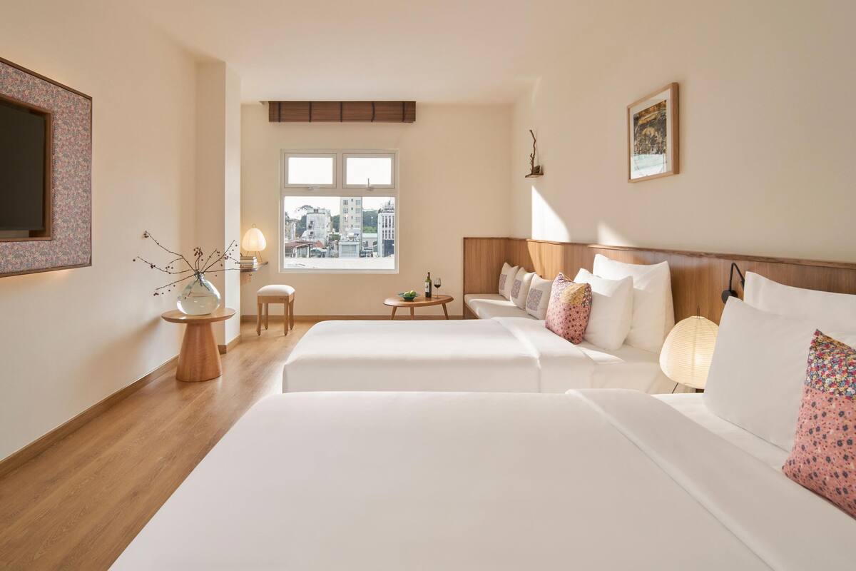 Una habitación de hotel con una cama grande, una mesita con lámpara, una ventana con vista a la ciudad y un cuadro en la pared.