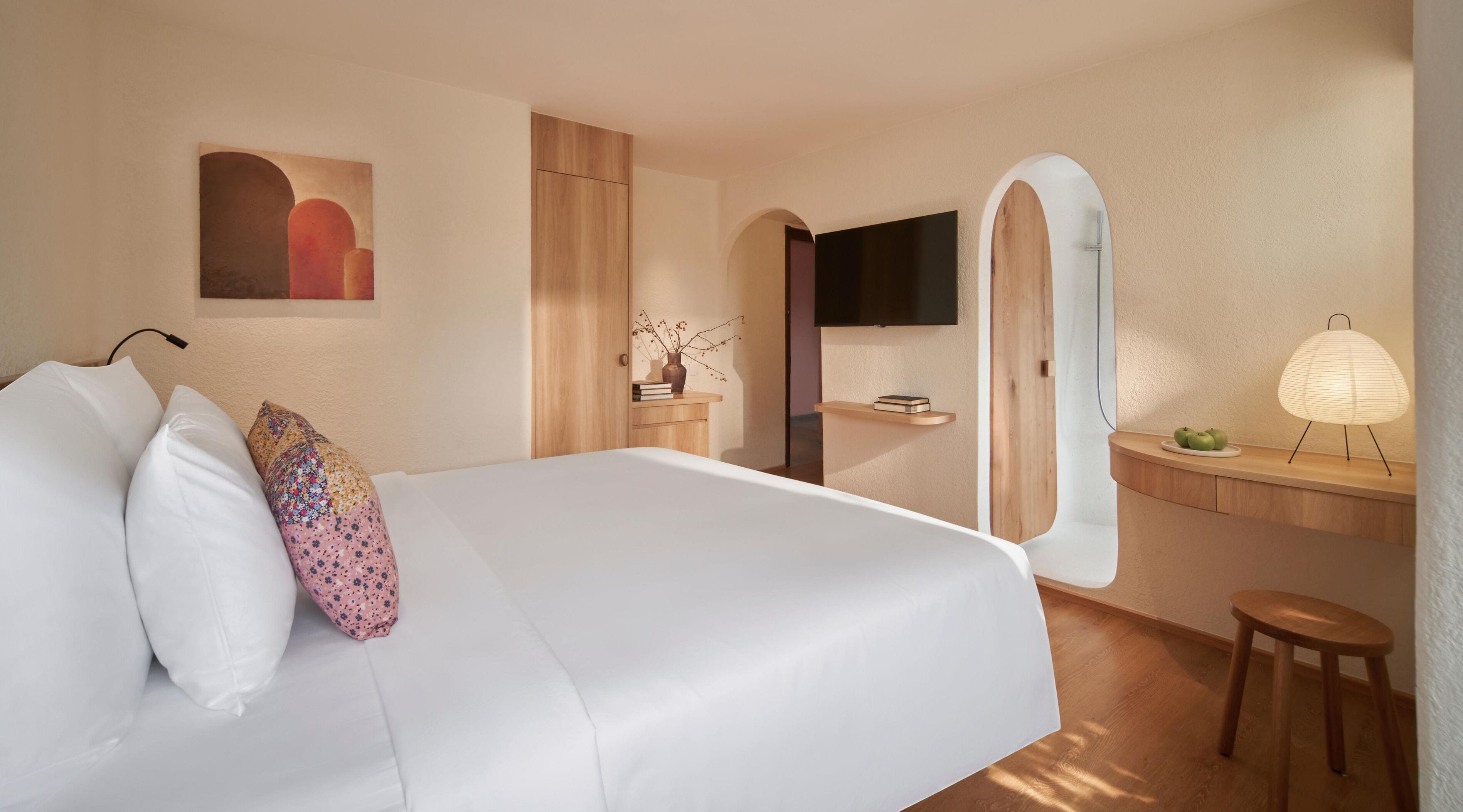 A modern hotel room with a large bed, a desk, a mirror, and a TV.