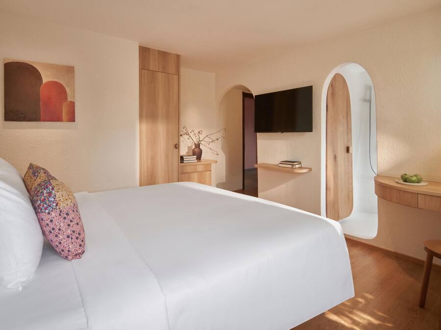 A modern hotel room with a large bed, a desk, a mirror, and a TV.