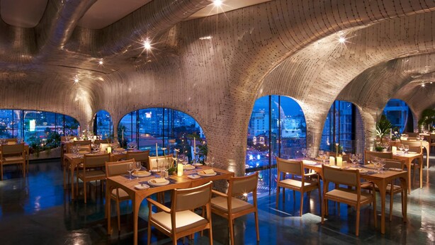 A modern restaurant with high ceilings and arched windows, offering a view of the cityscape at night. - Silverland Ben Thanh (Ho Chi Minh City)