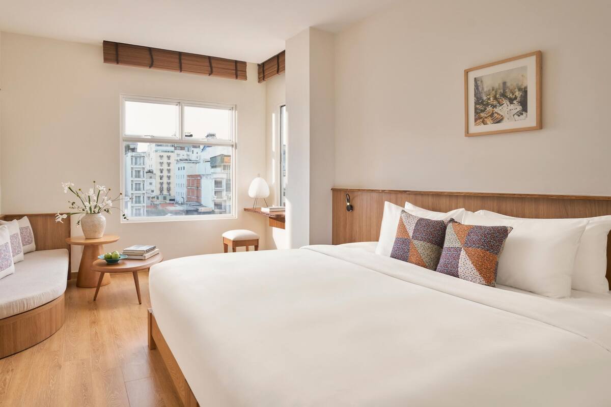 Habitación de hotel con una cama grande, una zona de estar con una mesita, un ventanal con vista a la ciudad y un cuadro en la pared.