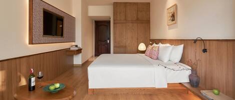 Habitación de hotel con una cama grande, un armario de madera, una mesita con una botella y vasos, y un cuadro en la pared.