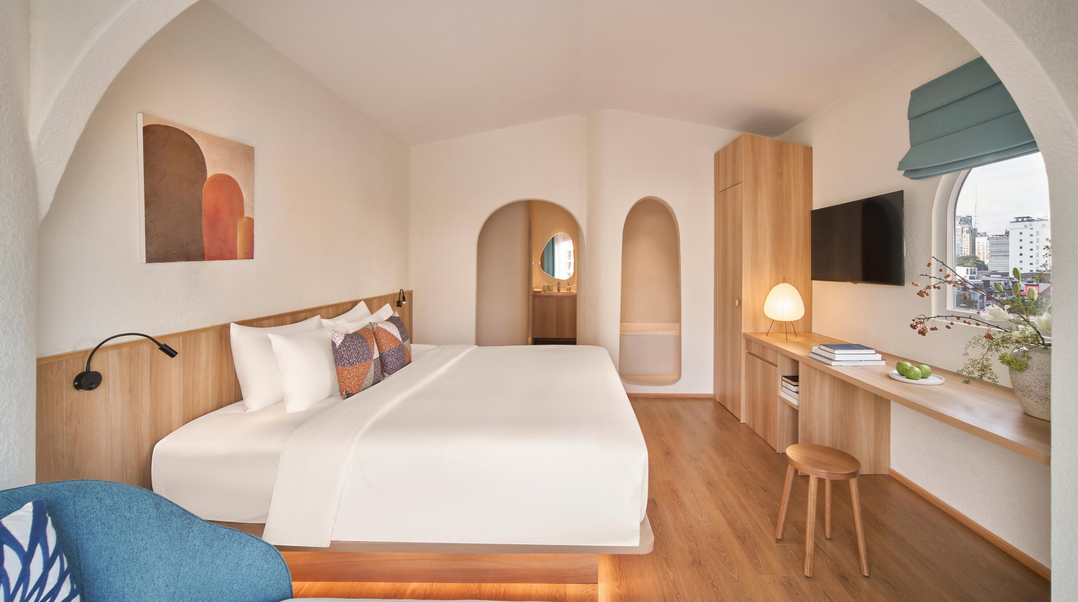 Et moderne hotelværelse med en stor seng, et skrivebord, et fjernsyn og et vindue med udsigt over byen.