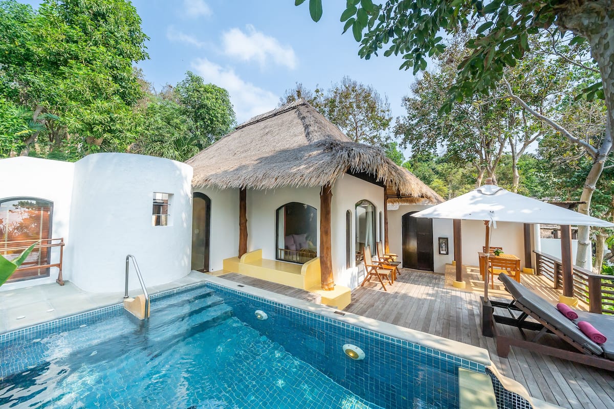 A pool area with a thatched-roof structure, lounge chairs, and a wooden deck.