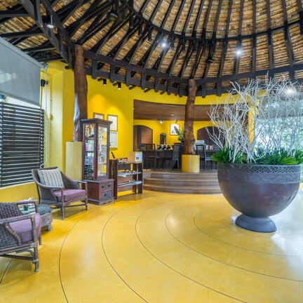A spacious lobby with a curved yellow floor, wicker furniture, a large decorative planter, and a thatched roof ceiling.