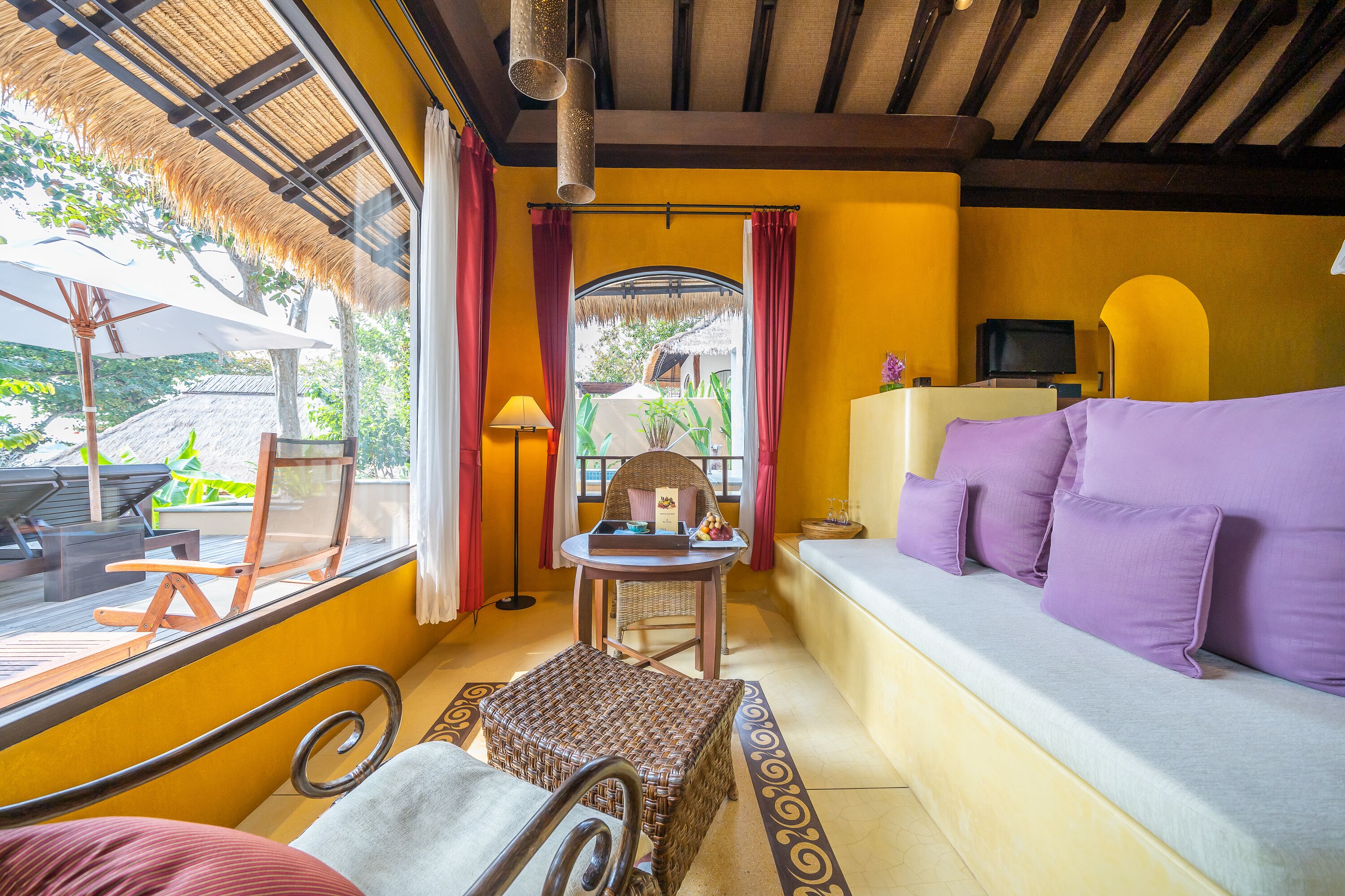 A cozy room with a sofa, a small table, a chair, and a window overlooking a garden.