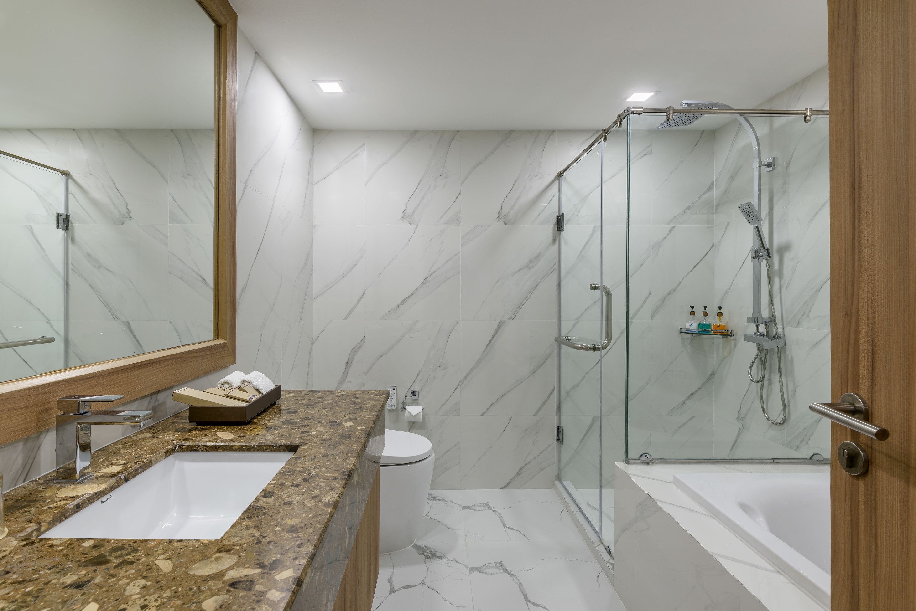 A modern bathroom with a marble wall, a sink, toilet, and a glass-enclosed shower.
