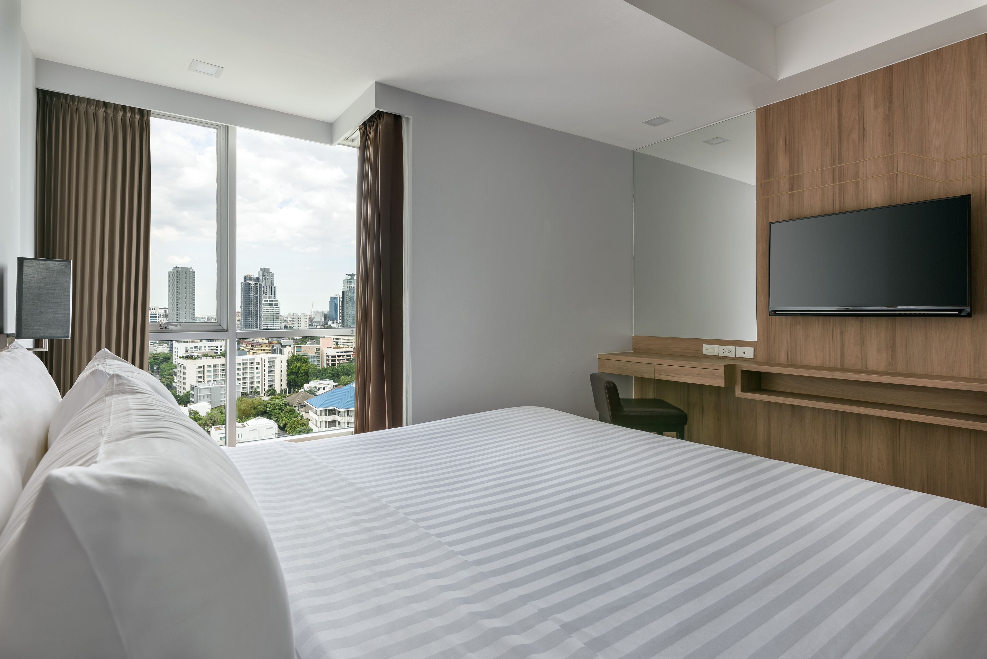 Une chambre d’hôtel avec un grand lit, un téléviseur fixé au mur et une vue sur la ville par la fenêtre.