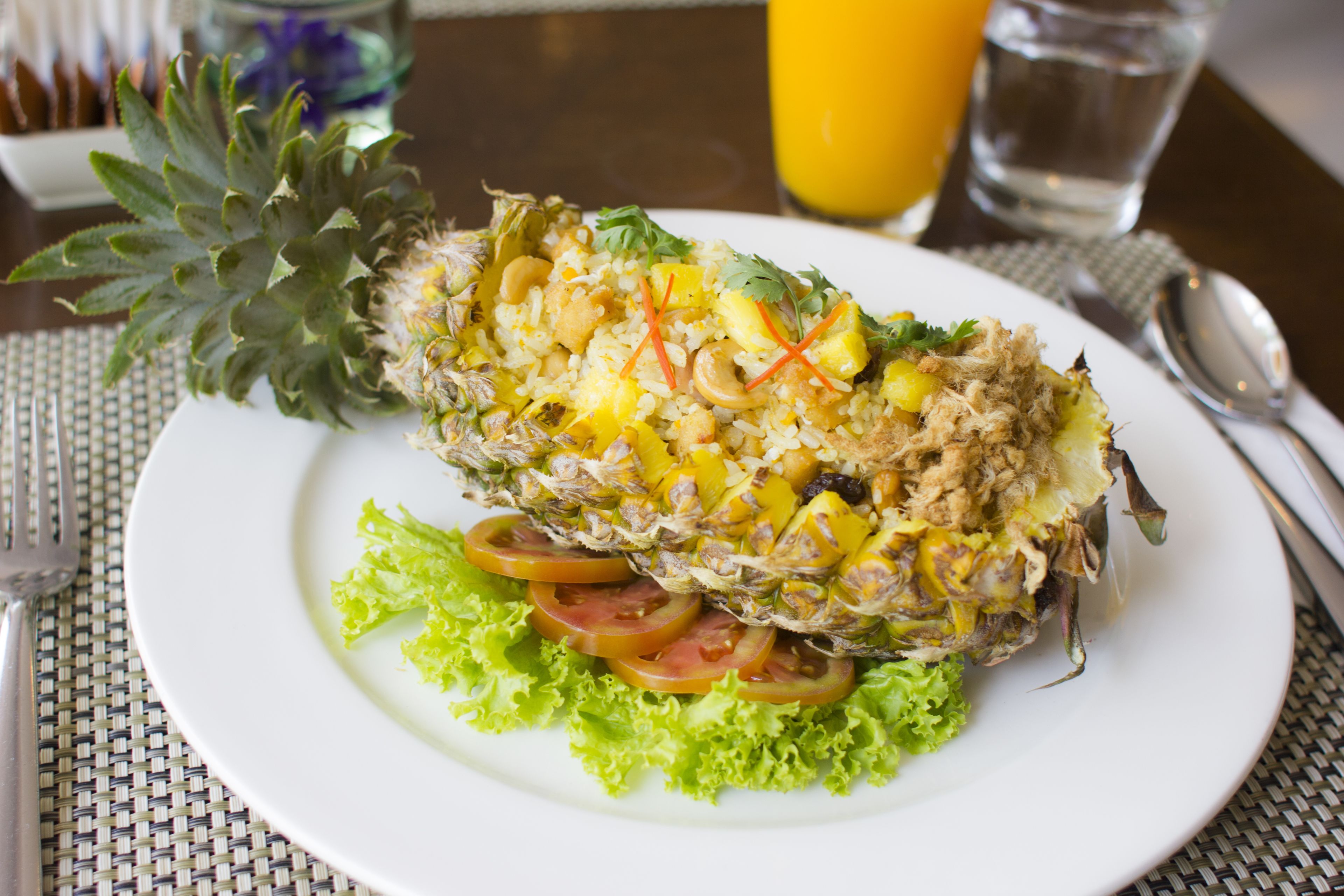 Une assiette blanche contenant un plat composé d’ananas, de riz et de légumes, avec une fourchette et une cuillère posées sur la table à côté.