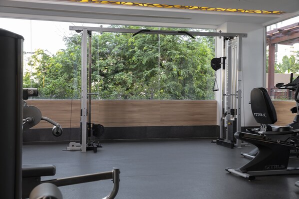 A gym with exercise equipment, a pull-up bar, and a view of trees through large windows.