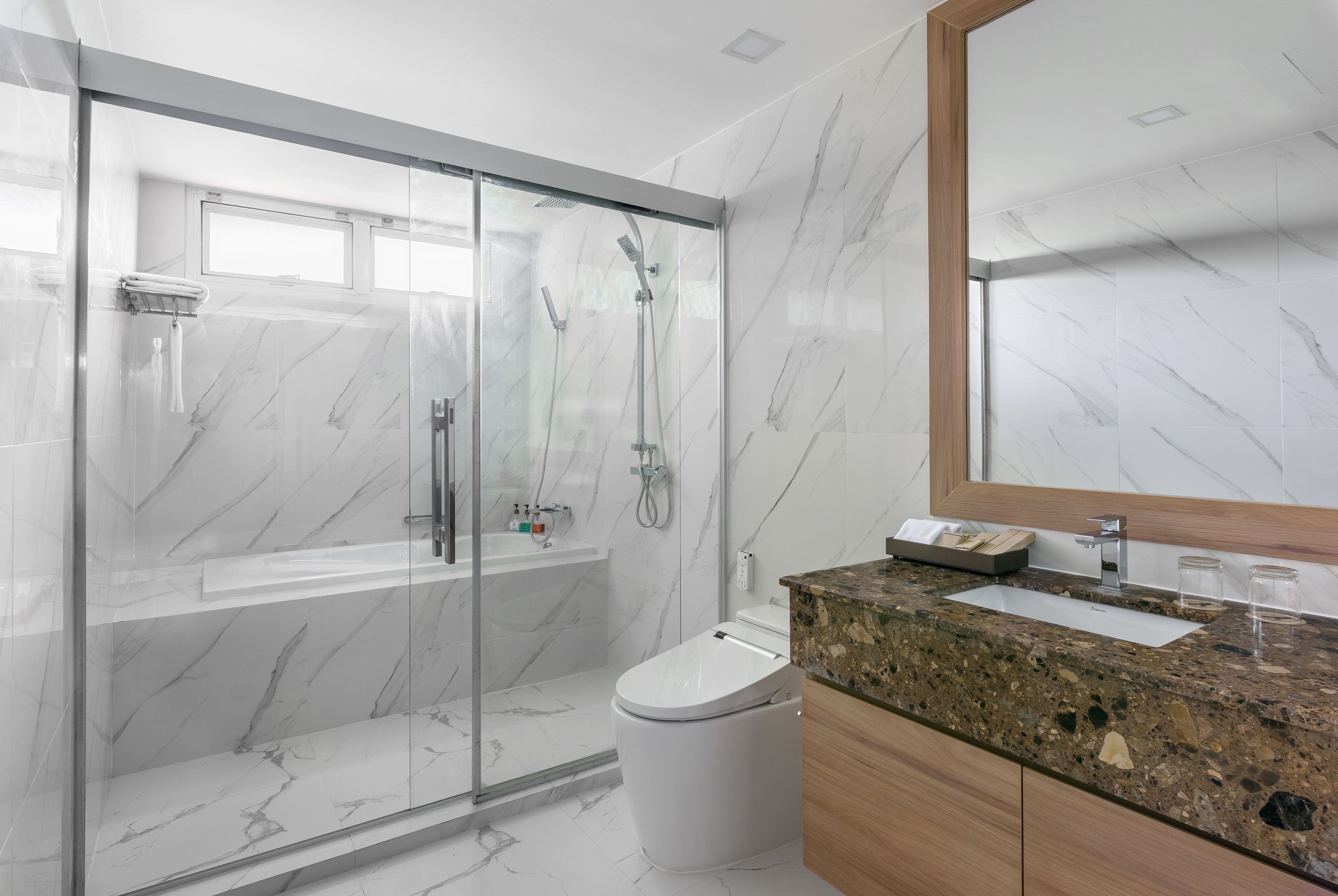 A modern bathroom with a glass-enclosed shower, a white toilet, and a granite countertop sink.