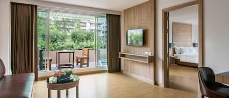 Una habitación de hotel moderna con piso de madera, un televisor de pantalla plana en la pared, una cama con ropa de cama blanca y un balcón con vista a follaje.