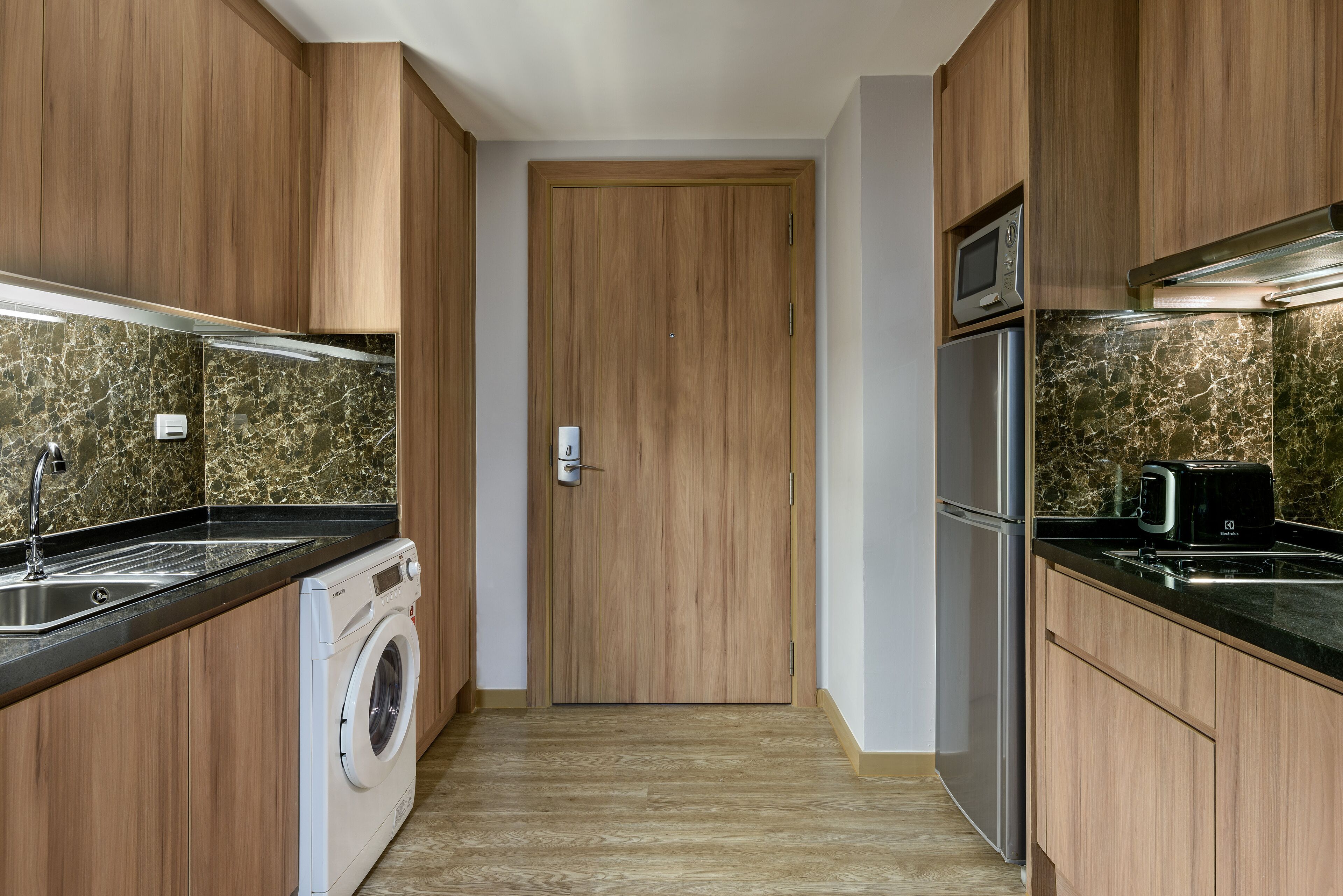 A compact kitchen with wooden cabinets, a washing machine, a microwave, and a toaster.