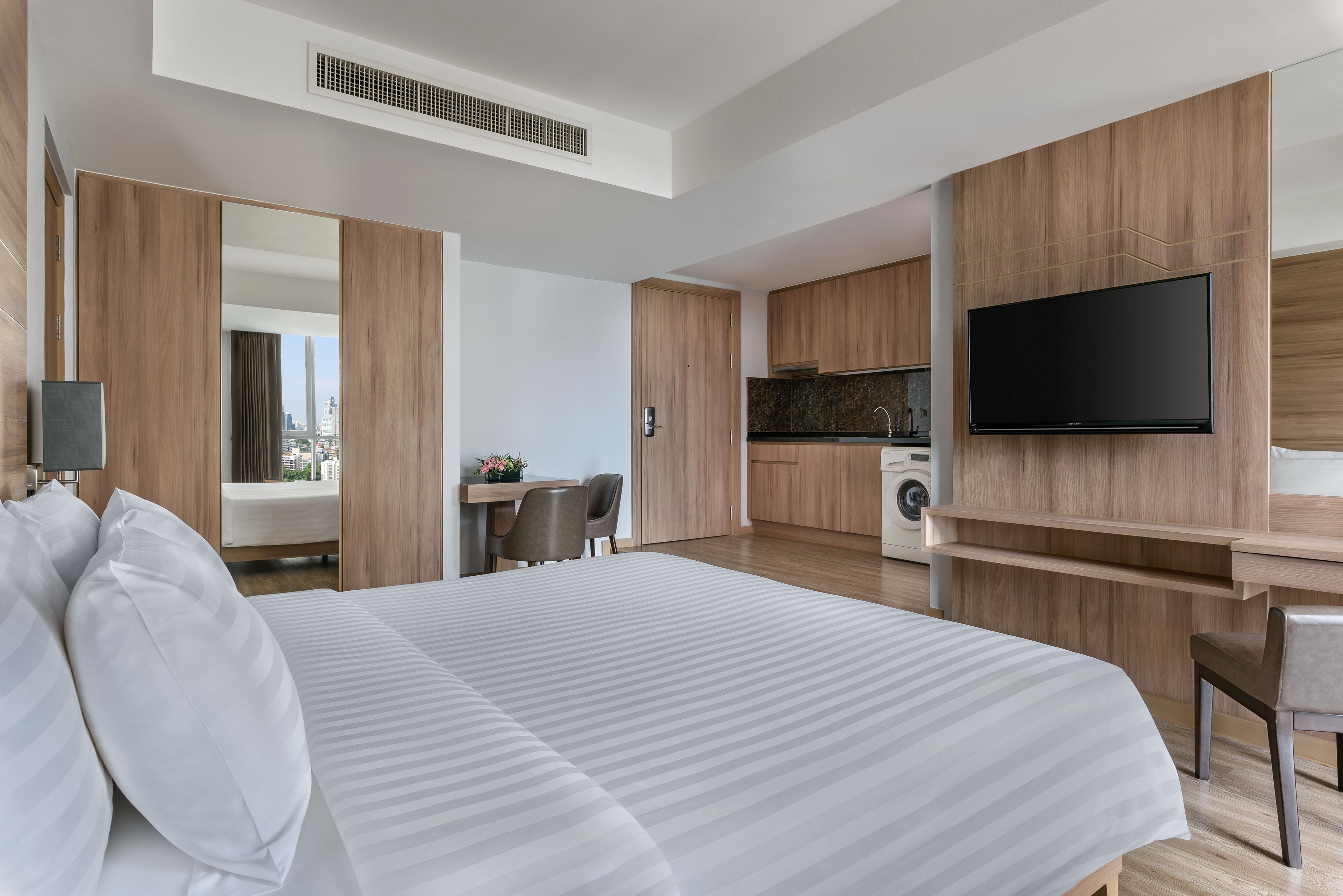 A modern hotel room with a large bed, a desk, a flat-screen TV, and a kitchenette.