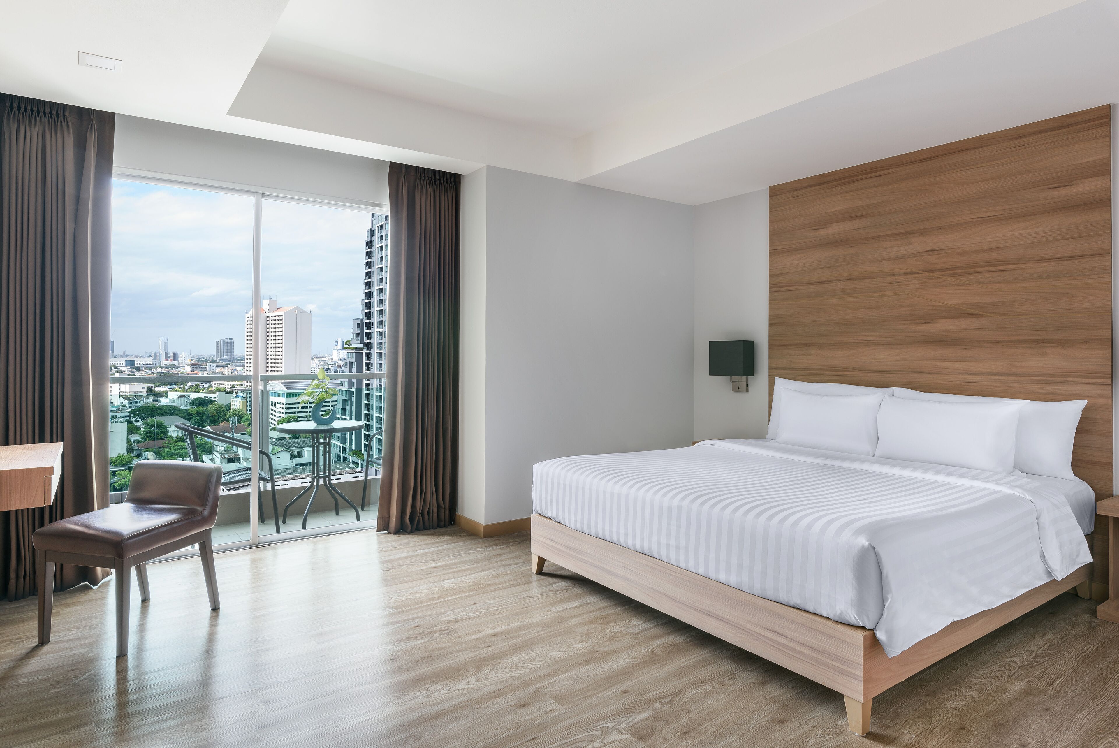 Ein modernes Hotelzimmer mit einem großen Bett, einem Schreibtisch und Blick auf die Stadt durch raumhohe Fenster.
