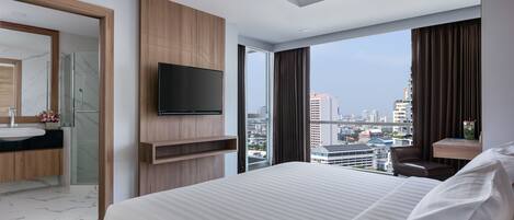 A modern hotel room with a large bed, a TV mounted on the wall, a bathroom with a mirror and sink, and a city view through large windows.