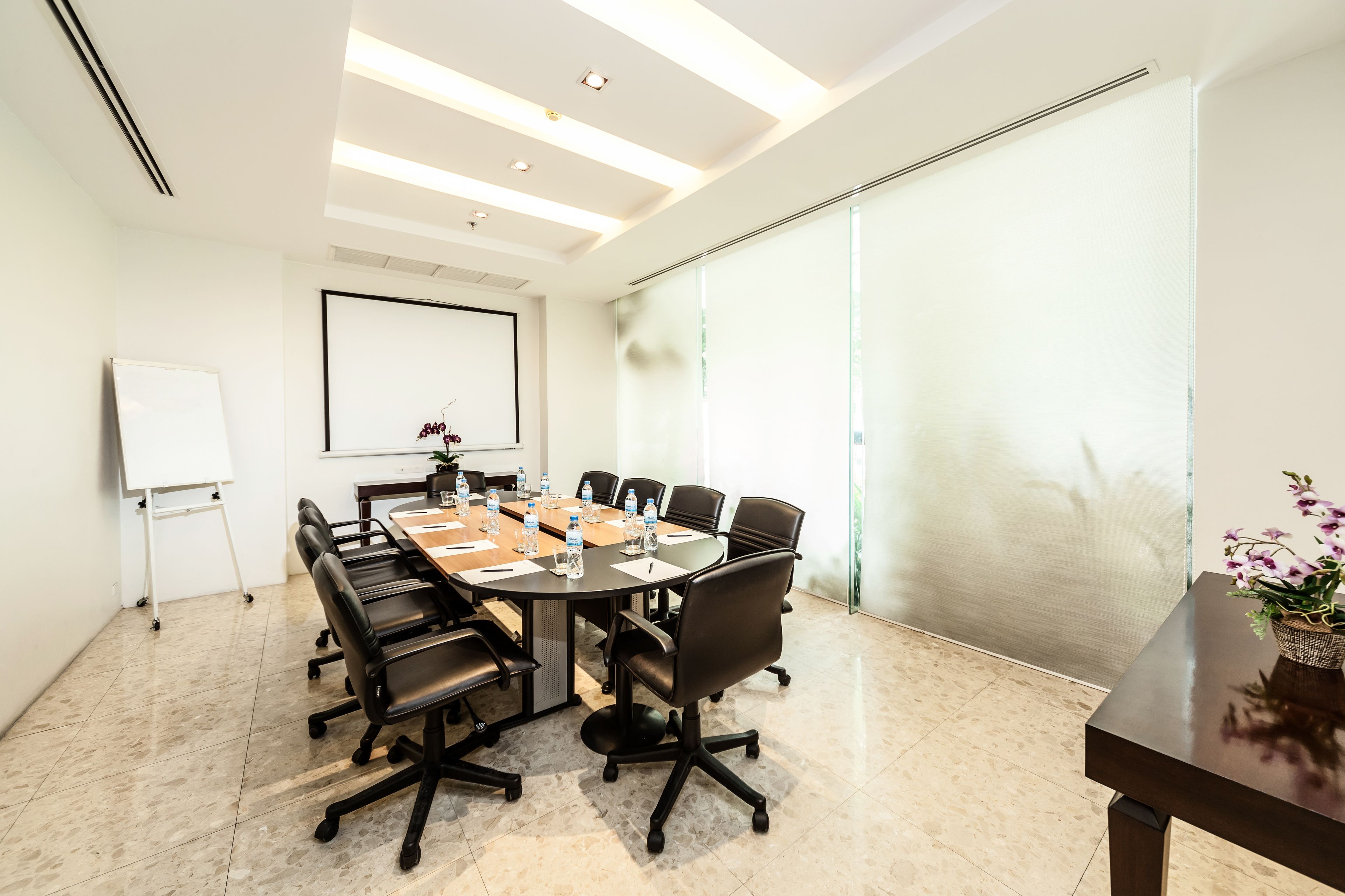 A conference room with a large table, black chairs, a whiteboard, and a projector screen.