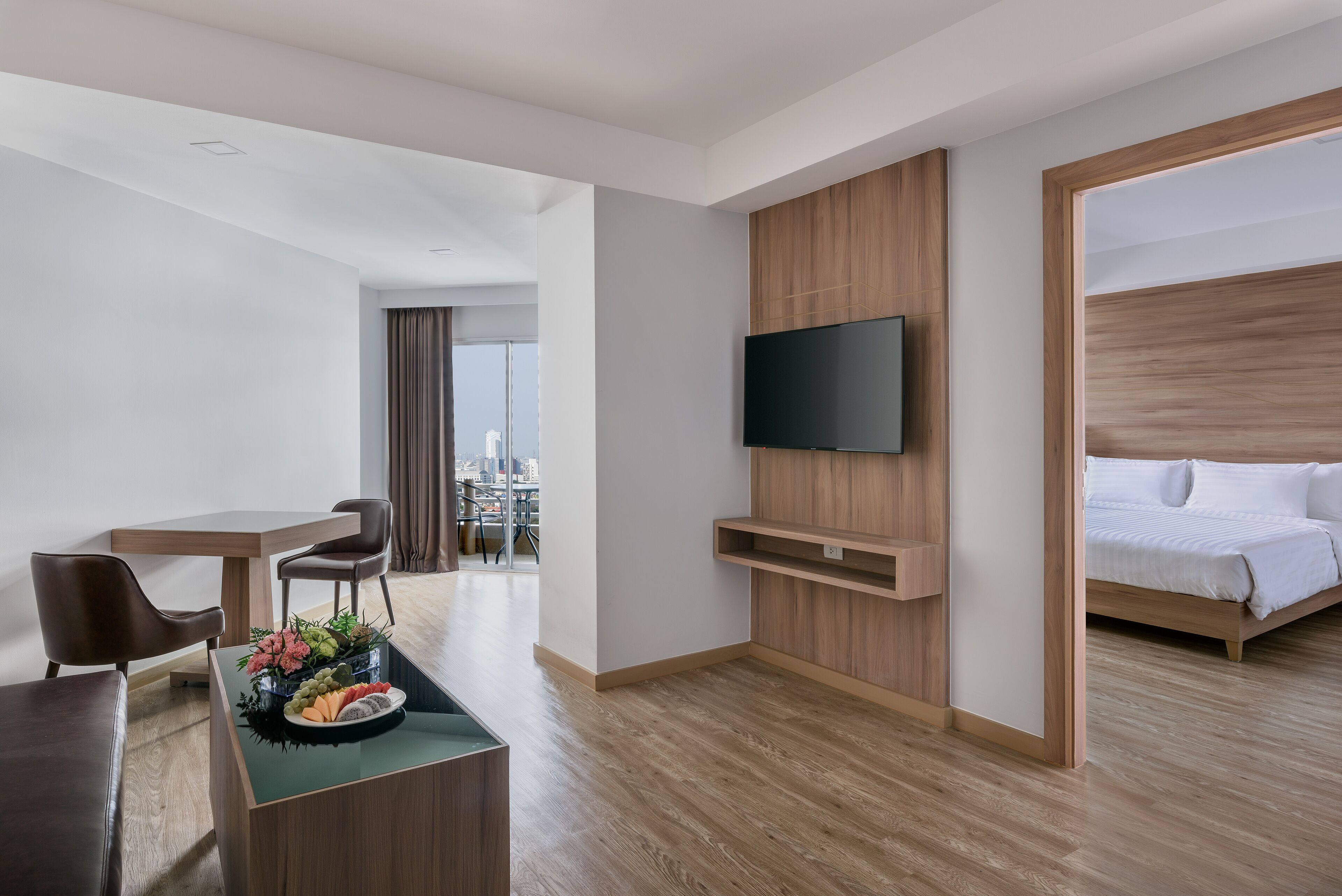 Een moderne hotelkamer met een bed, een bureau met stoelen, een flatscreen televisie aan de muur en uitzicht op de stad door grote ramen.