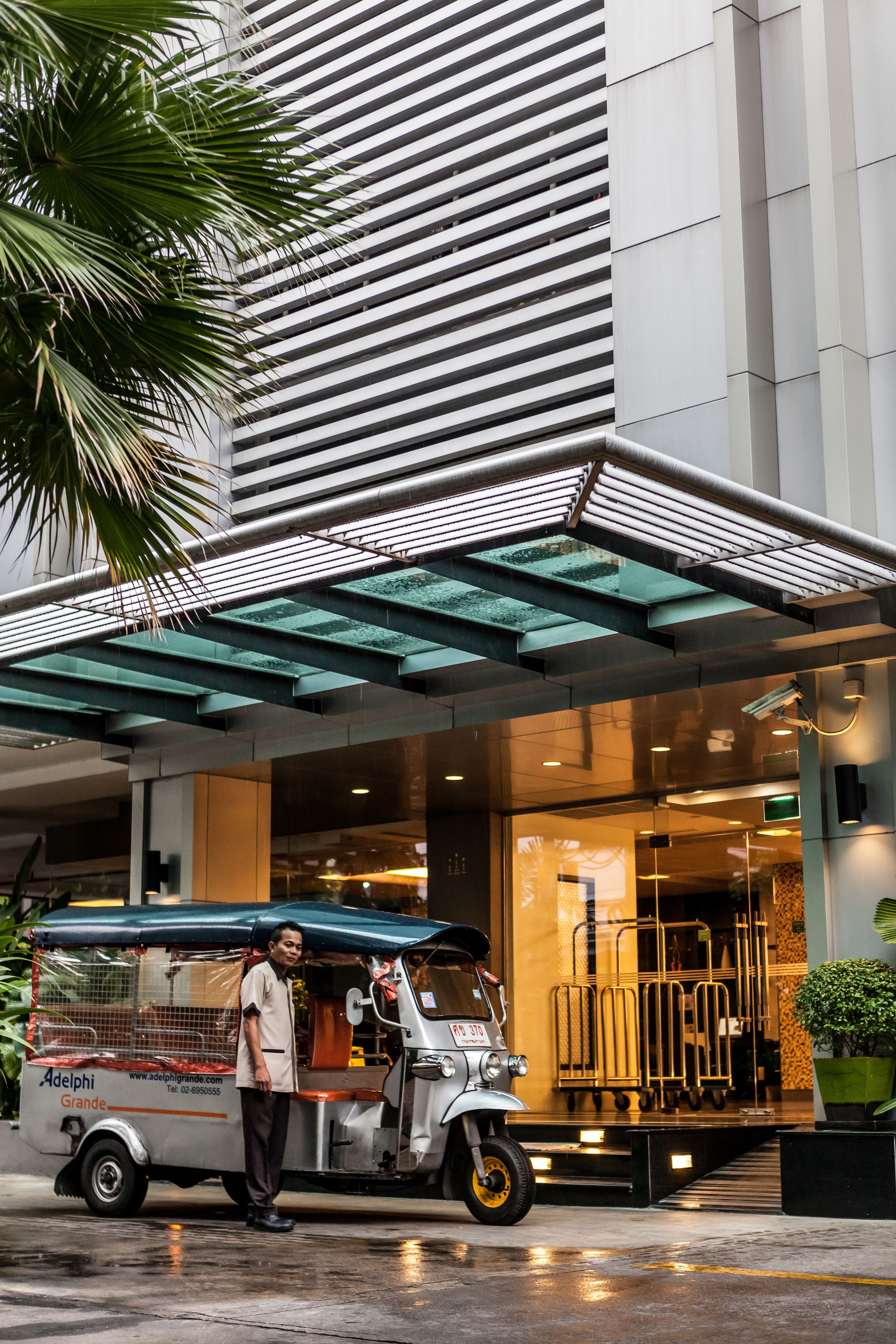 A tuk-tuk parked outside a building with a glass entrance and a metal awning.