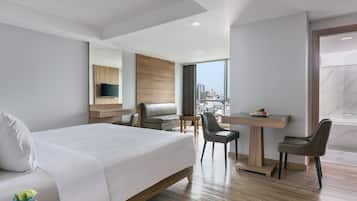 A modern hotel room with a large bed, a desk, two chairs, a TV, and a city view.