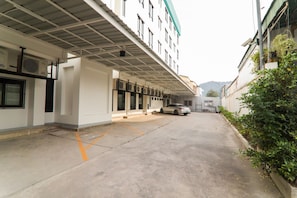 Uma área de estacionamento com um carro, uma cobertura e edifícios ao fundo.