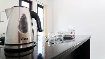 A kitchen area with a stainless steel moka pot labeled 'vista' and a coffee maker. There are two clear glass cups on the counter.
