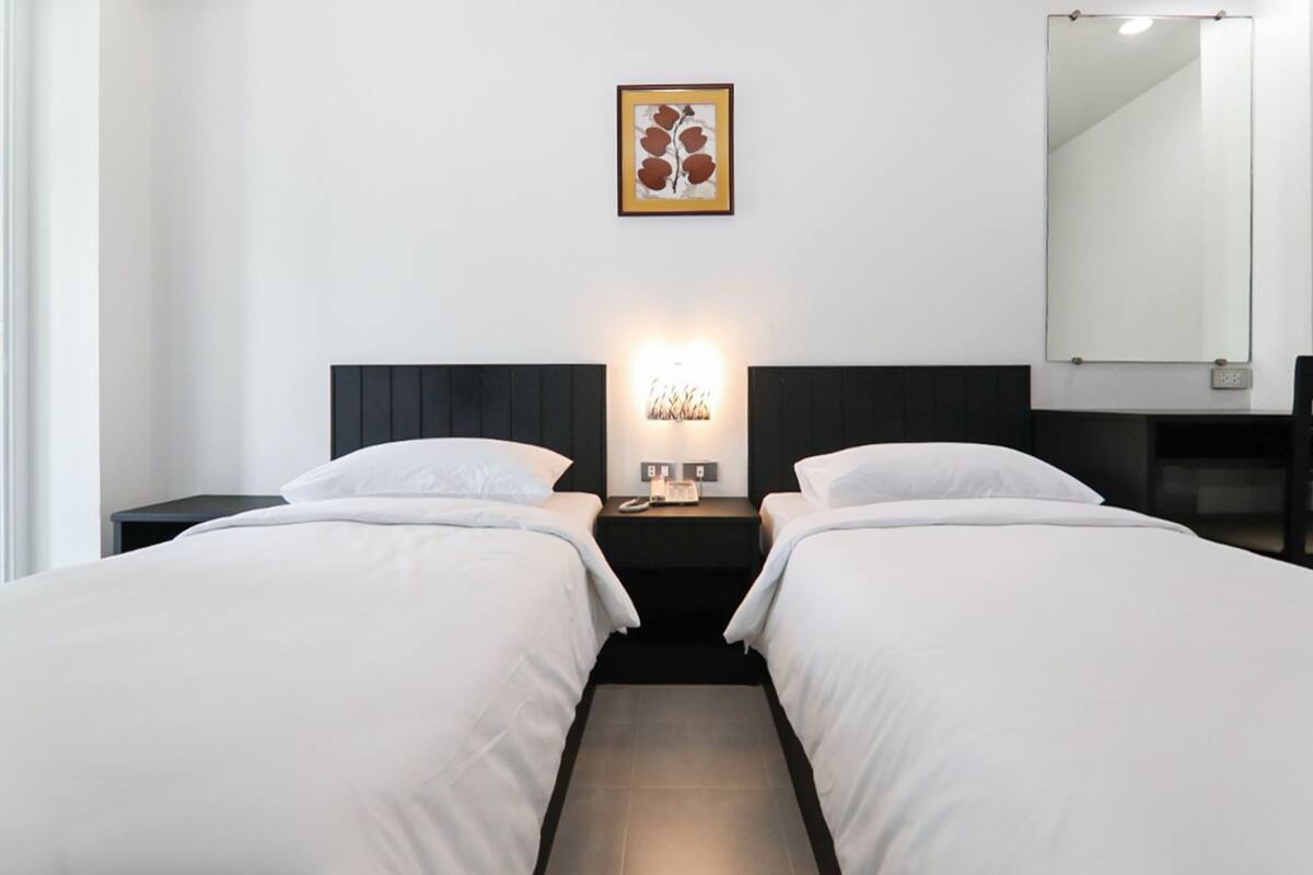 A hotel room with two beds, a nightstand with a lamp, a framed picture on the wall, and a large mirror.