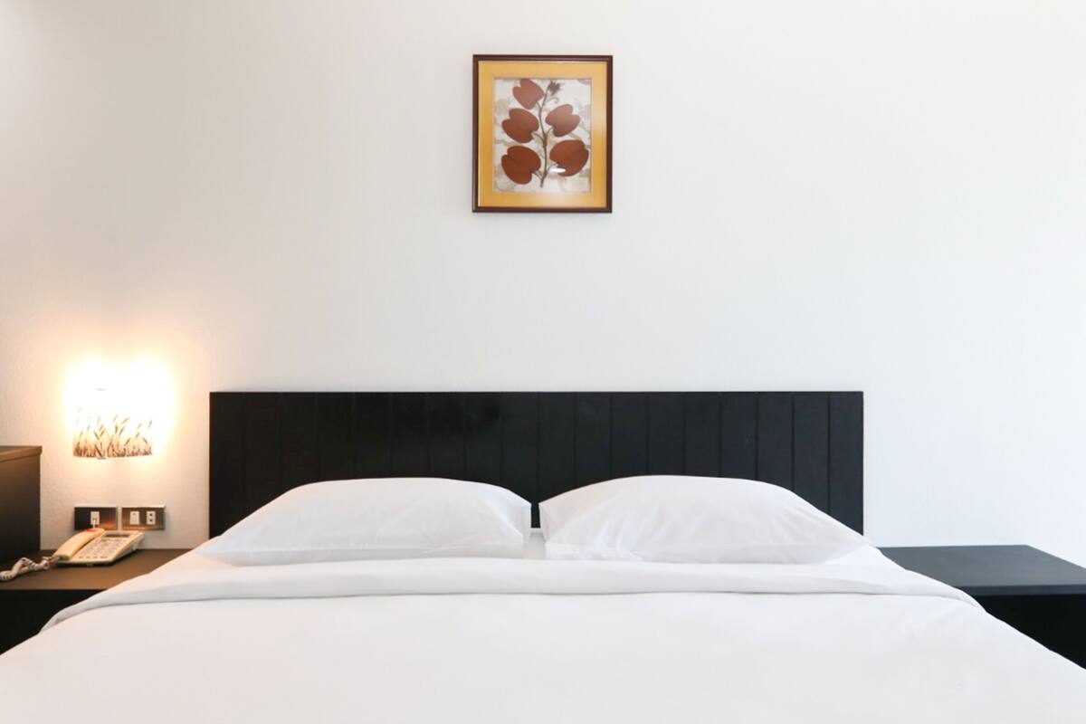 A hotel room with a bed, a nightstand with a lamp, and a framed artwork on the wall.