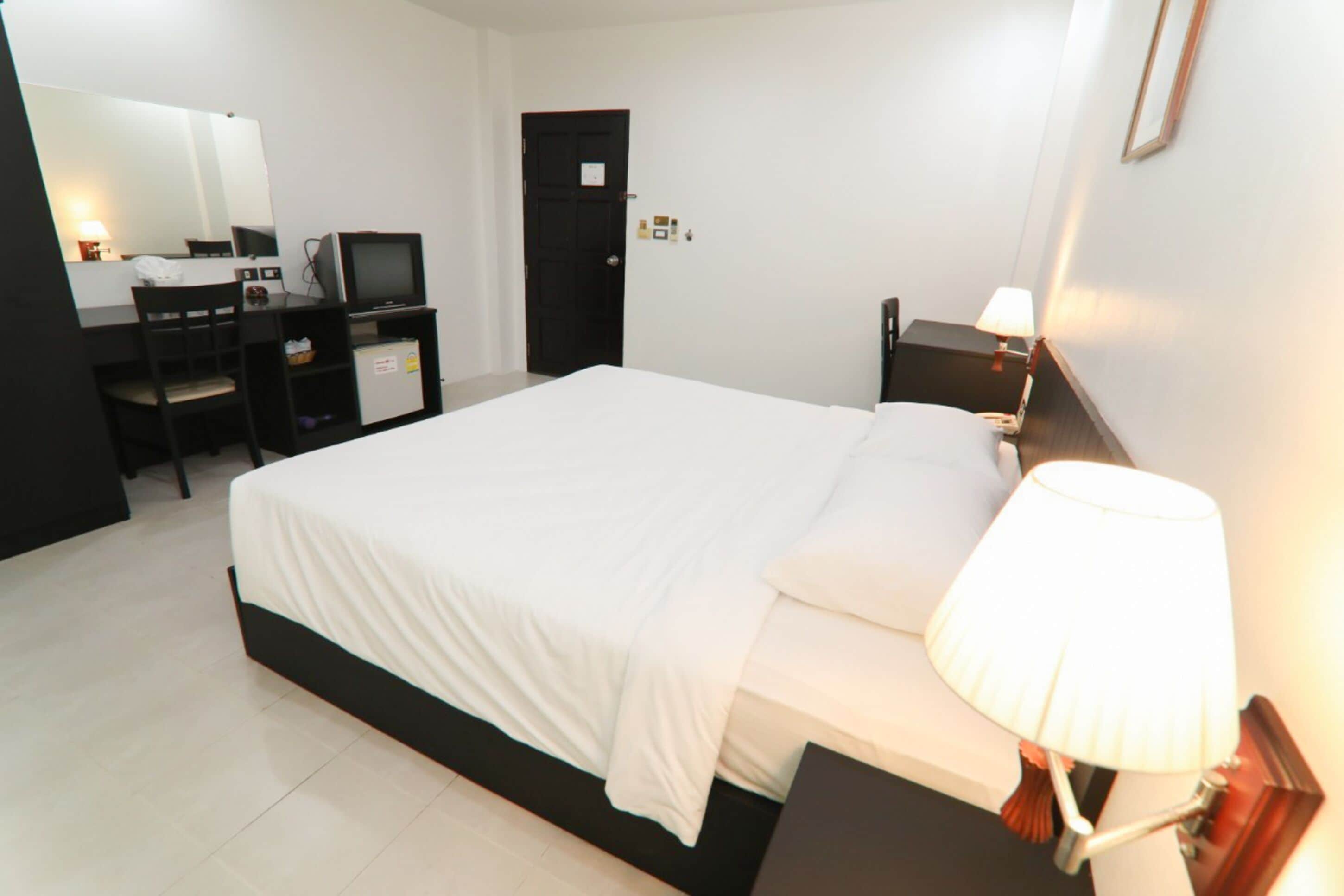 A hotel room with a bed, a desk with a computer, a chair, a TV, and a lamp.