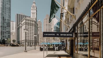 A hotel entrance with a sign reading 'CLUB QUARTERS 75 RIVER HOTEL' and a view of the city skyline in the background.