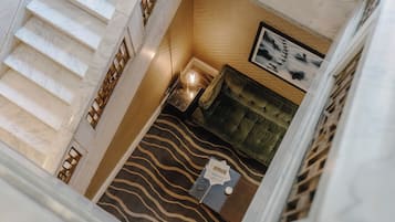Habitación de hotel con una escalera de mármol, alfombra estampada, sofá tapizado en verde y una pequeña mesa con lámpara.