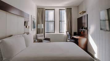 A hotel room with a large bed, a desk, a chair, a TV, and a window with curtains.