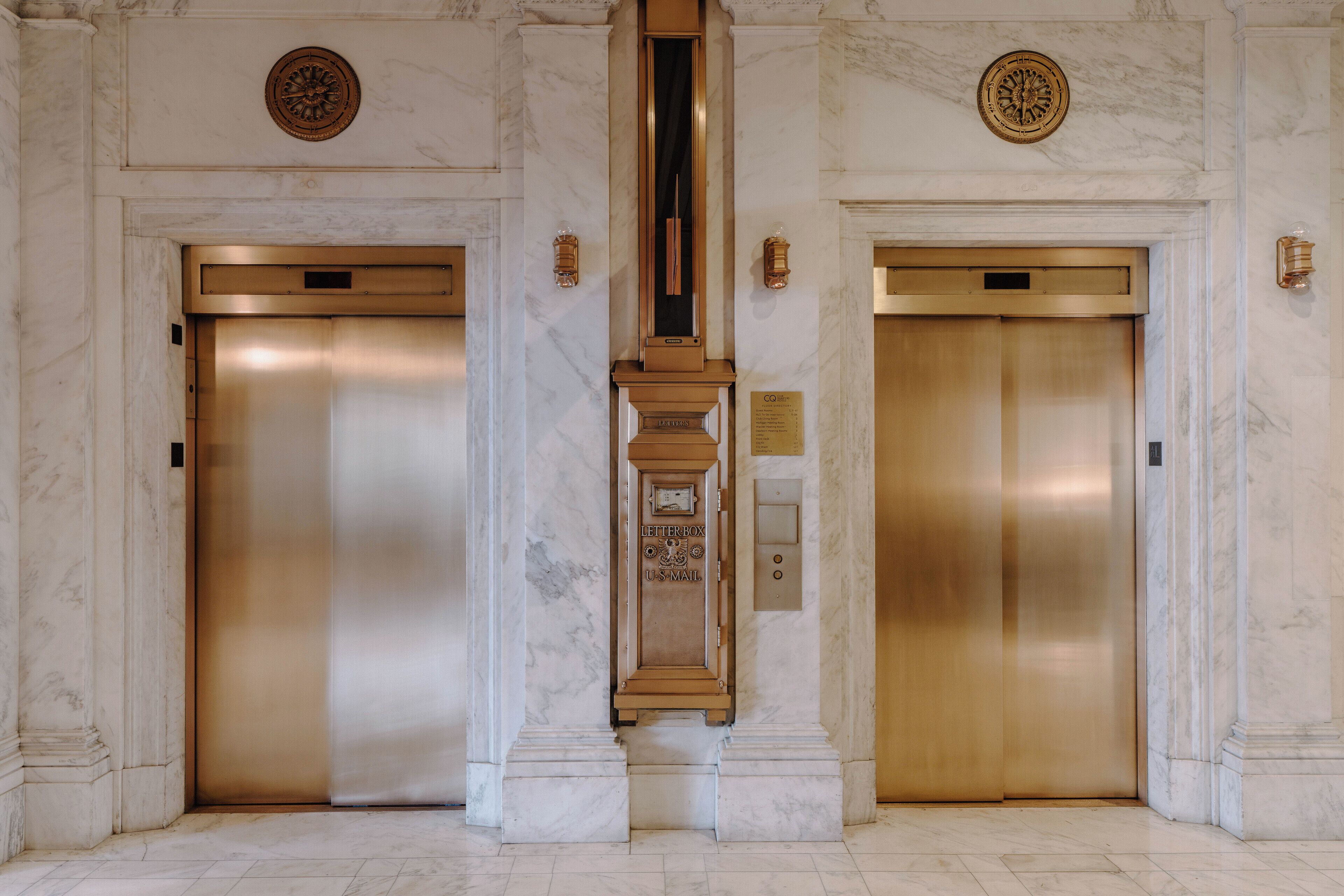 Two elevators in a marble-floored lobby with a central column and decorative elements.