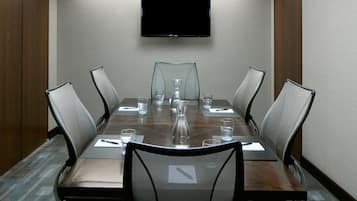 Un salón de conferencias con una larga mesa, seis sillas, un televisor montado en la pared y una alfombra estampada.