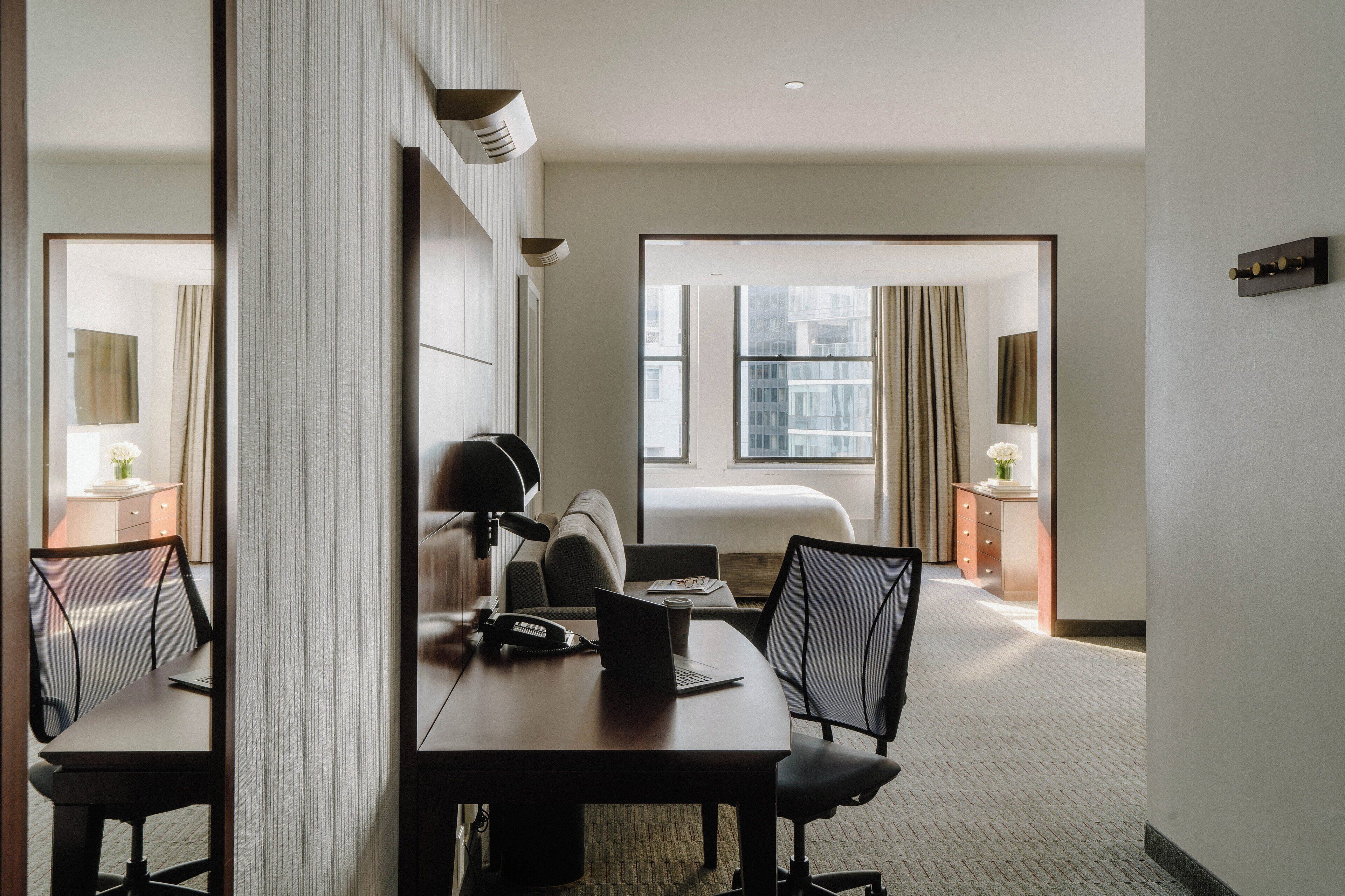 Une chambre d’hôtel équipée d’un bureau, de chaises, d’un lit et offrant une vue sur la ville.