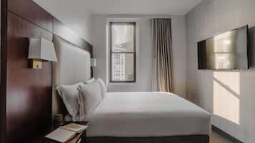 Quarto de hotel com uma cama grande, mesa de cabeceira com abajur, televisão de tela plana na parede e uma janela com cortinas.