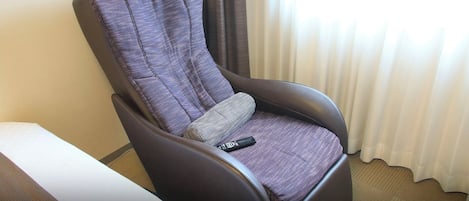 A reclining chair with a remote control, a pillow, and a window with curtains.