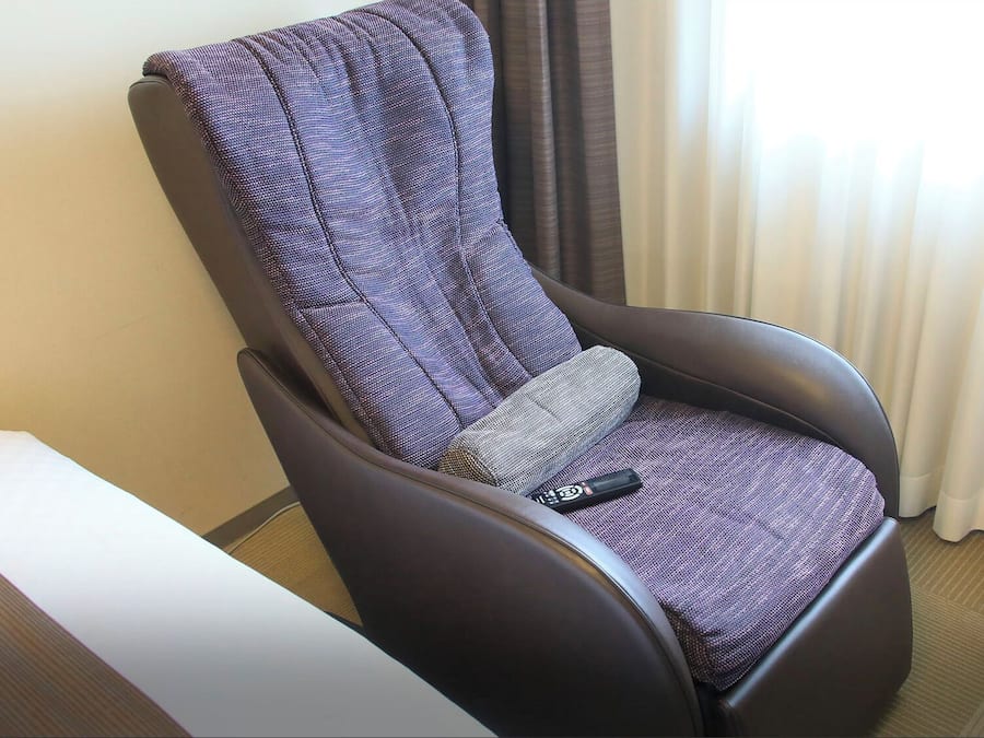 A reclining chair with a remote control, a pillow, and a window with curtains.