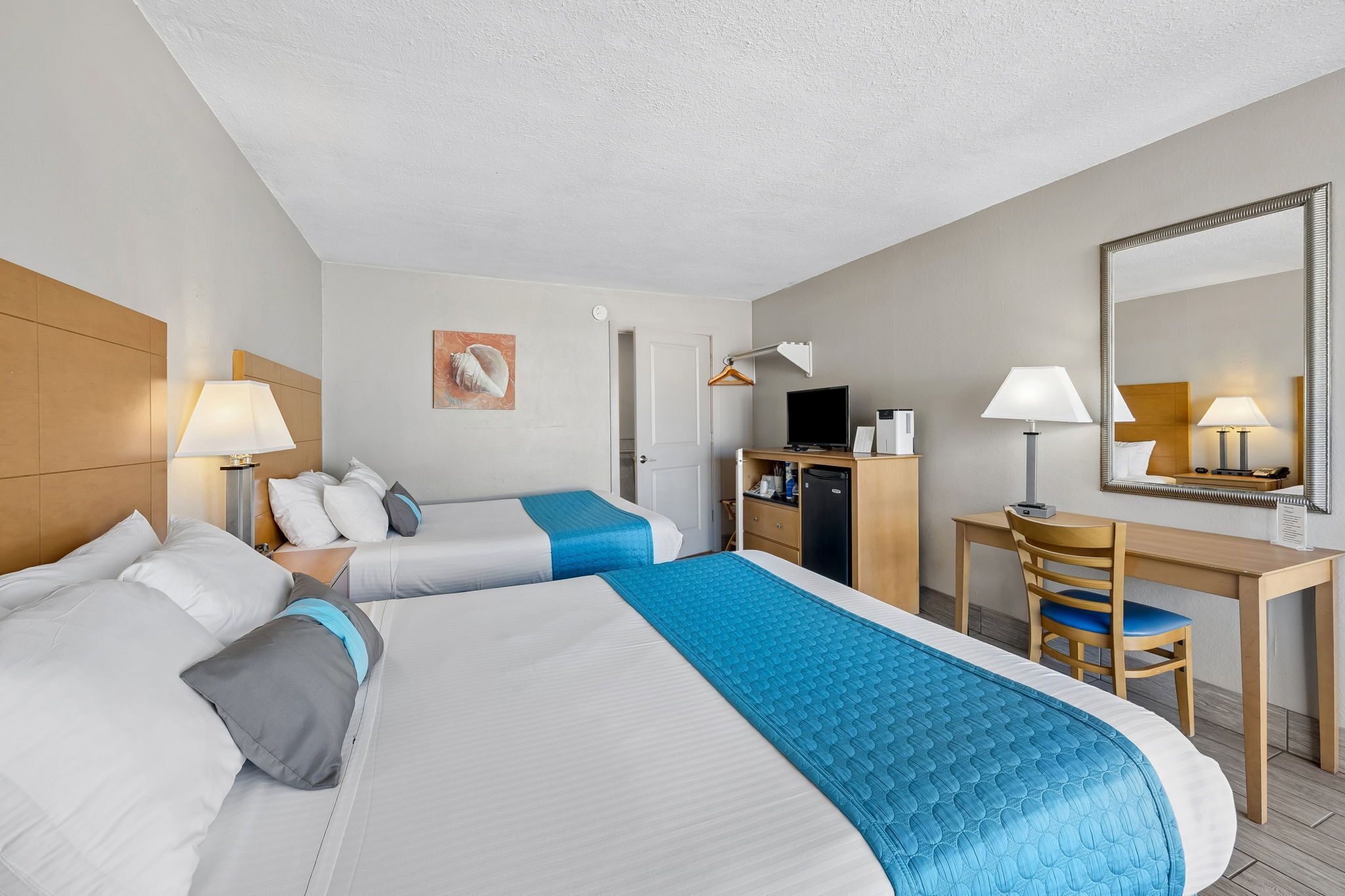 A hotel room with two beds, a desk, a chair, a TV, and a mirror.