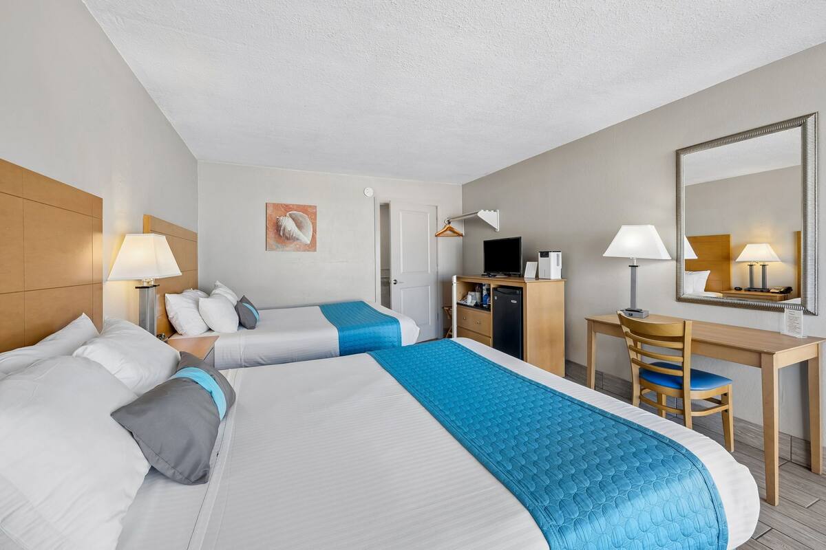A hotel room with two beds, a desk, a chair, a TV, and a mirror.
